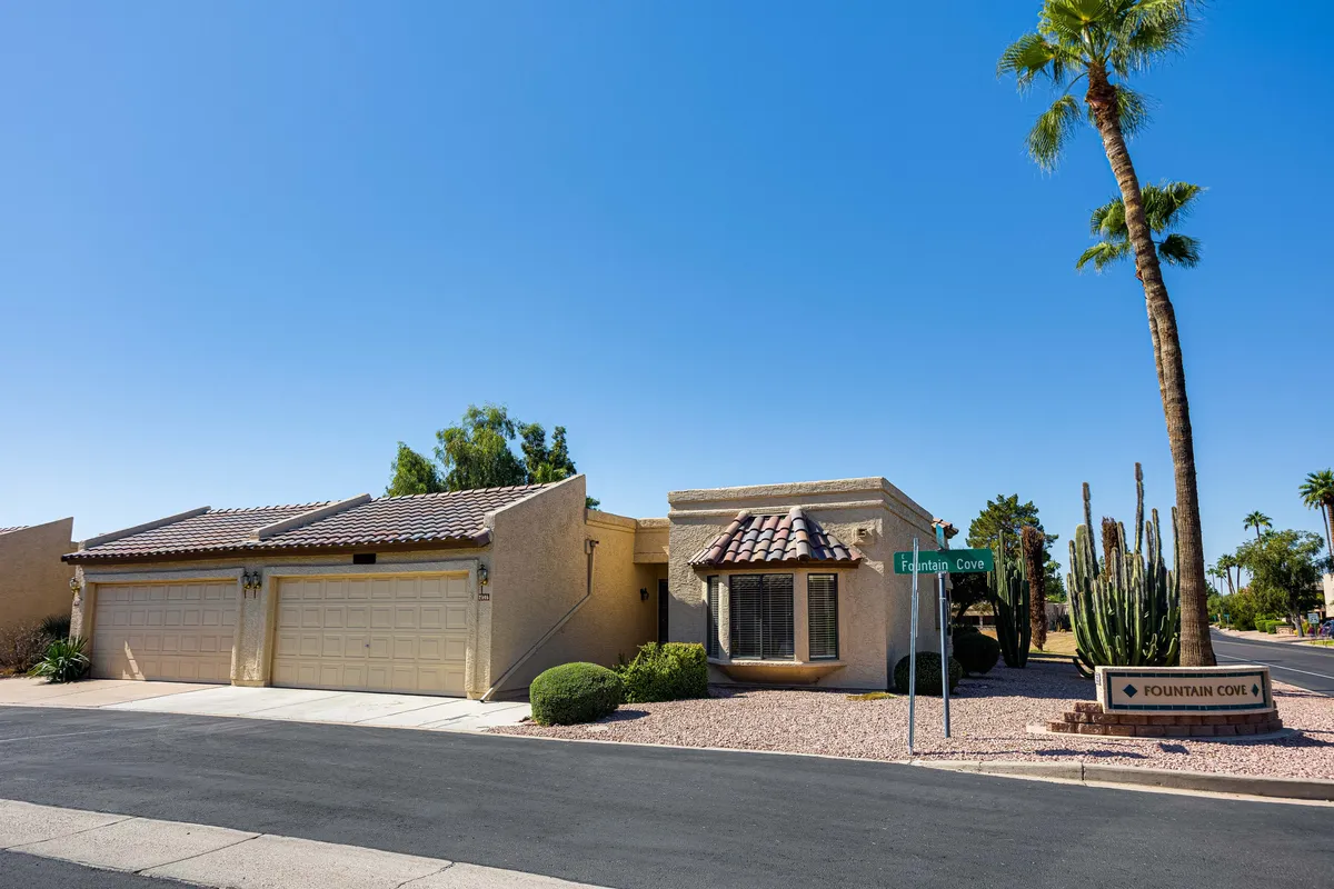 The main entrance of the house is surrounded by palm trees and cacti, with a visible street sign suggesting a friendly, walkable neighborhood. The scene feels open and welcoming, inviting guests and their pets to explore the area together.