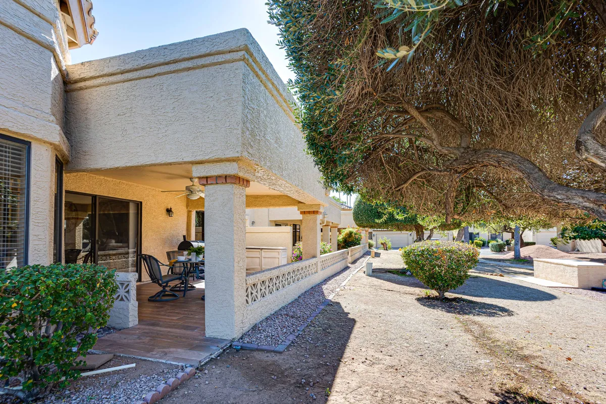 A covered patio with comfortable outdoor seating overlooks lush greenery and a decorative stone pathway. The space feels tranquil and welcoming, ideal for enjoying the Arizona weather, reading, hosting friends, or relaxing in the shade.