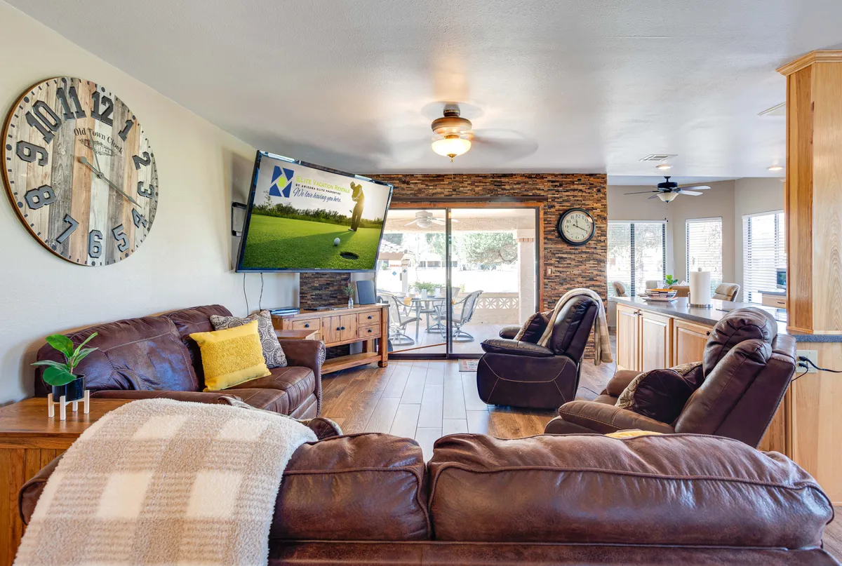Here, a comfortable living room features leather sofas, a large flat-screen television set into a stone accent wall, and a view toward the dining table. The rich wood finishes and elegant decor convey warmth and sophistication, while the layout encourages both relaxation and social interaction.