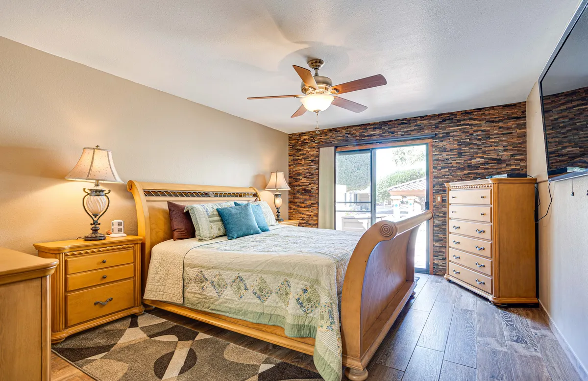 This image features a serene bedroom with a sleigh bed, decorative pillows, nightstands, and a large window allowing abundant natural light. The calm, cozy atmosphere emphasizes the room as a restful retreat, ideal for unwinding after an active day. The stone accent wall and soft ambient lighting add an elegant touch.