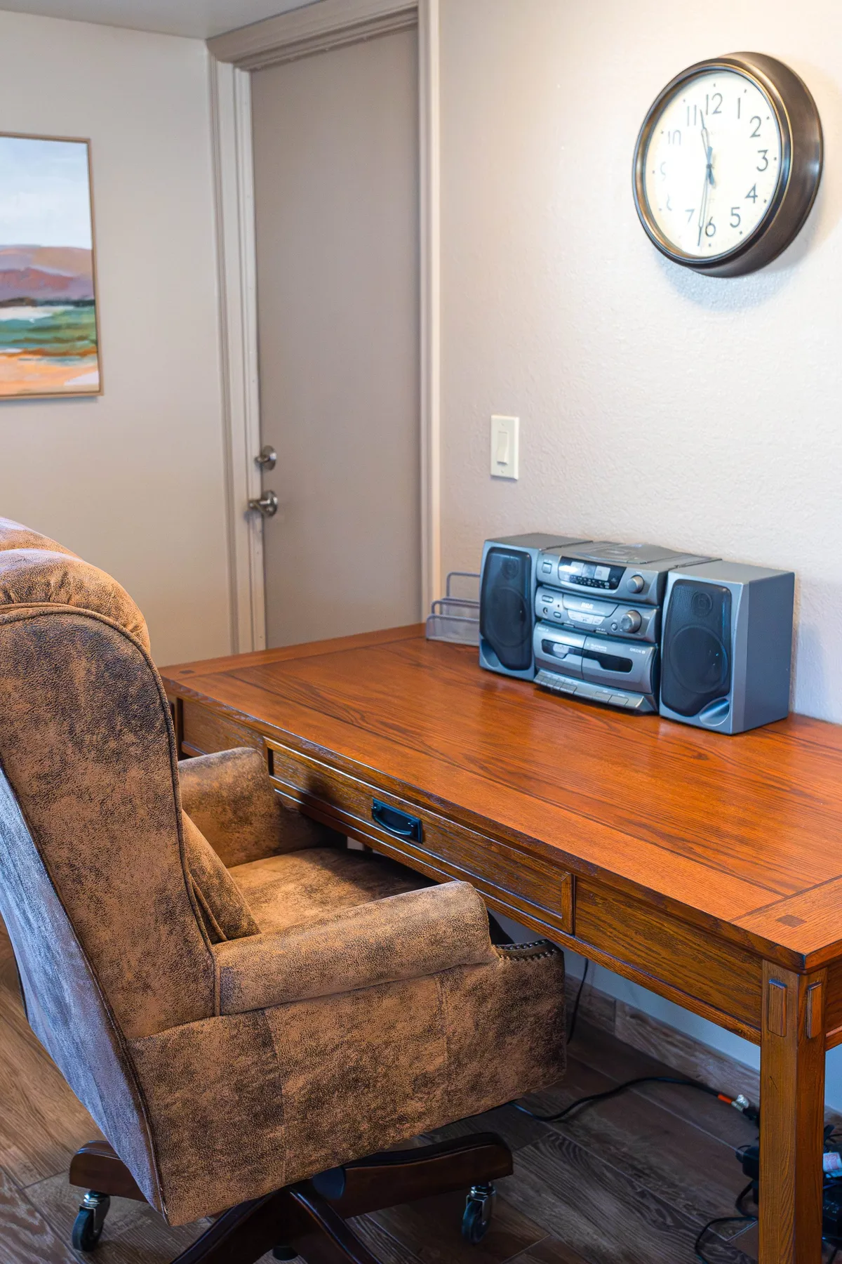 A cozy workspace with a wooden desk, comfortable chair, stereo system, and wall art, set in a well-lit part of the home. The setup encourages productivity in a warm, homey environment.