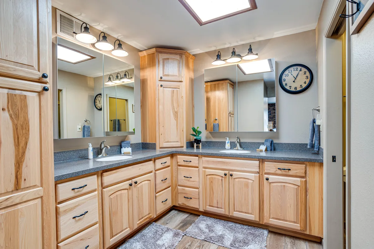 A stylish, organized bathroom with wooden cabinetry, mirrored surfaces, ample lighting, and a calm ambiance. The space clearly supports personal grooming and relaxation, echoing the spa-like qualities mentioned in the suite details.