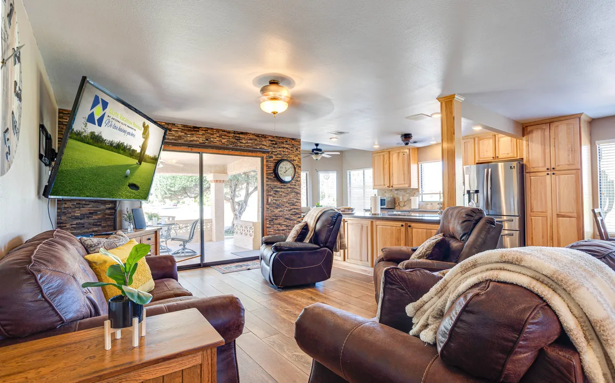 An inviting living area featuring comfortable leather couches, a large flat-screen TV, and a kitchen visible in the background. The space is ideal for family movie nights, relaxed socializing, or gathering before heading out to explore Mesa.
