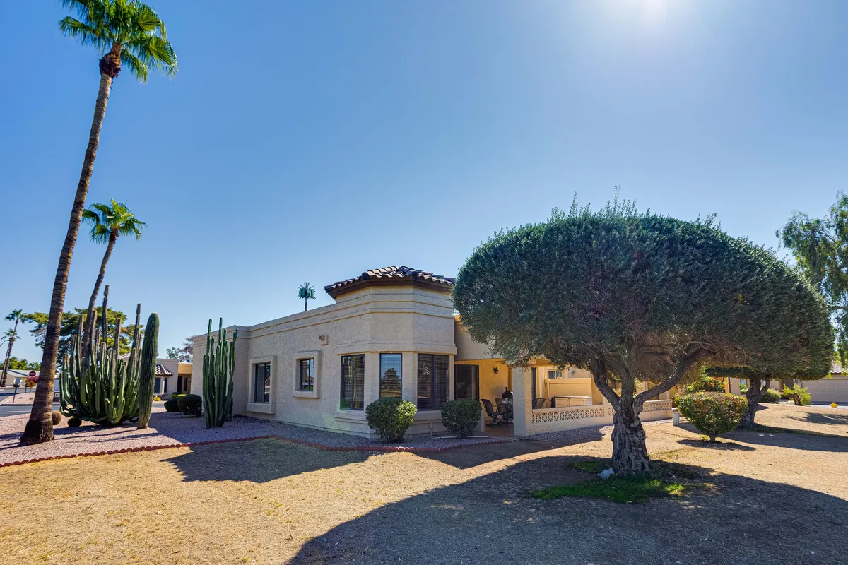 The home's exterior facade is framed by large trees, palm trees, and cacti, creating a lush, welcoming atmosphere. The yard offers space for relaxation and outdoor activities, with ample room for strolls and play.