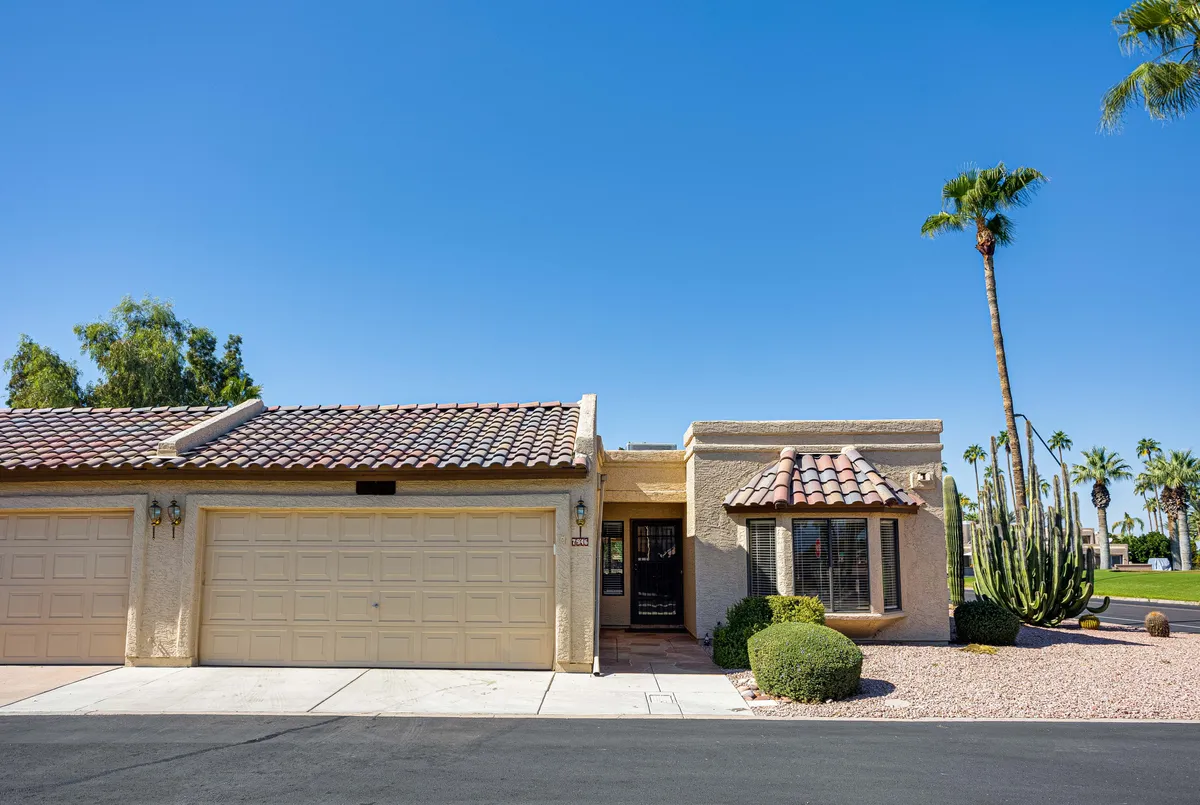 This image displays the welcoming front entrance of the home, featuring well-maintained landscaping, palm trees, and garage doors. The vibrant Arizona sunshine highlights the inviting exterior and the sense of a safe, friendly neighborhood.