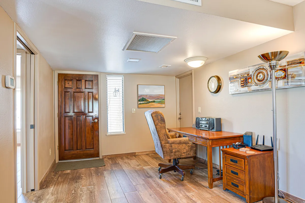 A cozy workspace featuring a wooden desk and chair, brightened by wall art and a lamp. Positioned near a doorway, it offers a quiet nook for productivity—ideal for remote work or planning the next adventure.