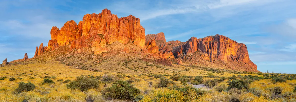 A sweeping view of striking desert rock formations under a vivid blue sky, surrounded by golden shrubs. The landscape invites exploration and outdoor adventure, reminiscent of local attractions such as Usery Mountain Regional Park and the Desert Botanical Garden.