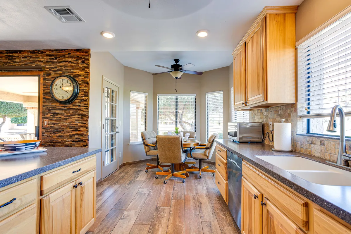 A cozy dining area adjoins the kitchen, featuring a round table surrounded by comfortable chairs and set against a stone accent wall. Large windows draw in natural light, while the seamless transition between kitchen and dining space highlights the open-concept layout.