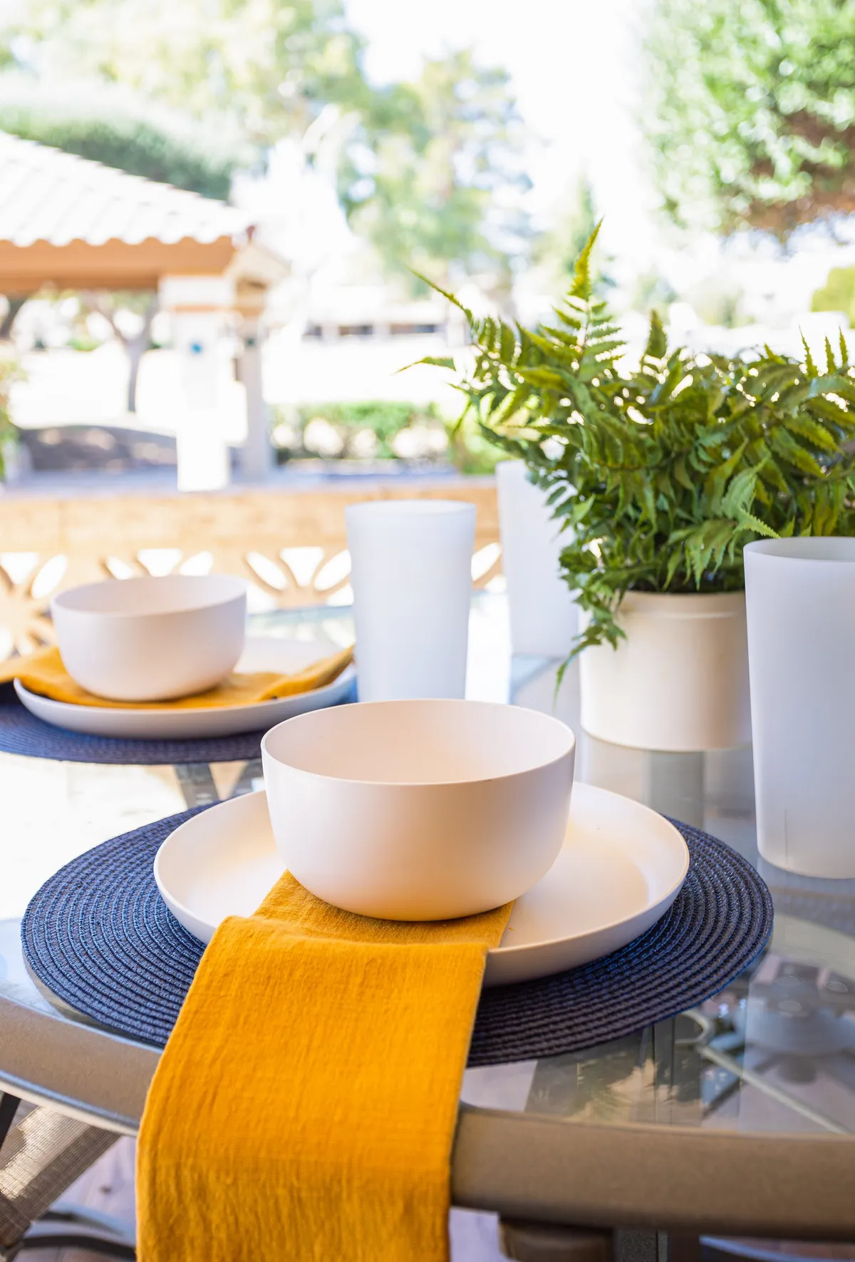 This image features a cheerful outdoor dining setting, complete with a table adorned with white bowls, a yellow table runner, and a lush green plant centerpiece. The setup is on a patio, suggesting a space where families can gather for meals, socialize, or enjoy the fresh air.